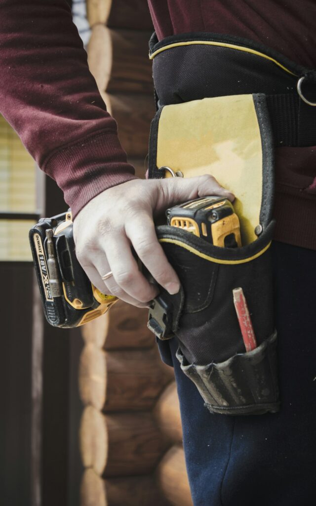 person-holding-black-and-yellow-nike-gloves-yqgpsbllpz0 Satisfied worker is drilling wall. Builder is working construction site. Wooden house